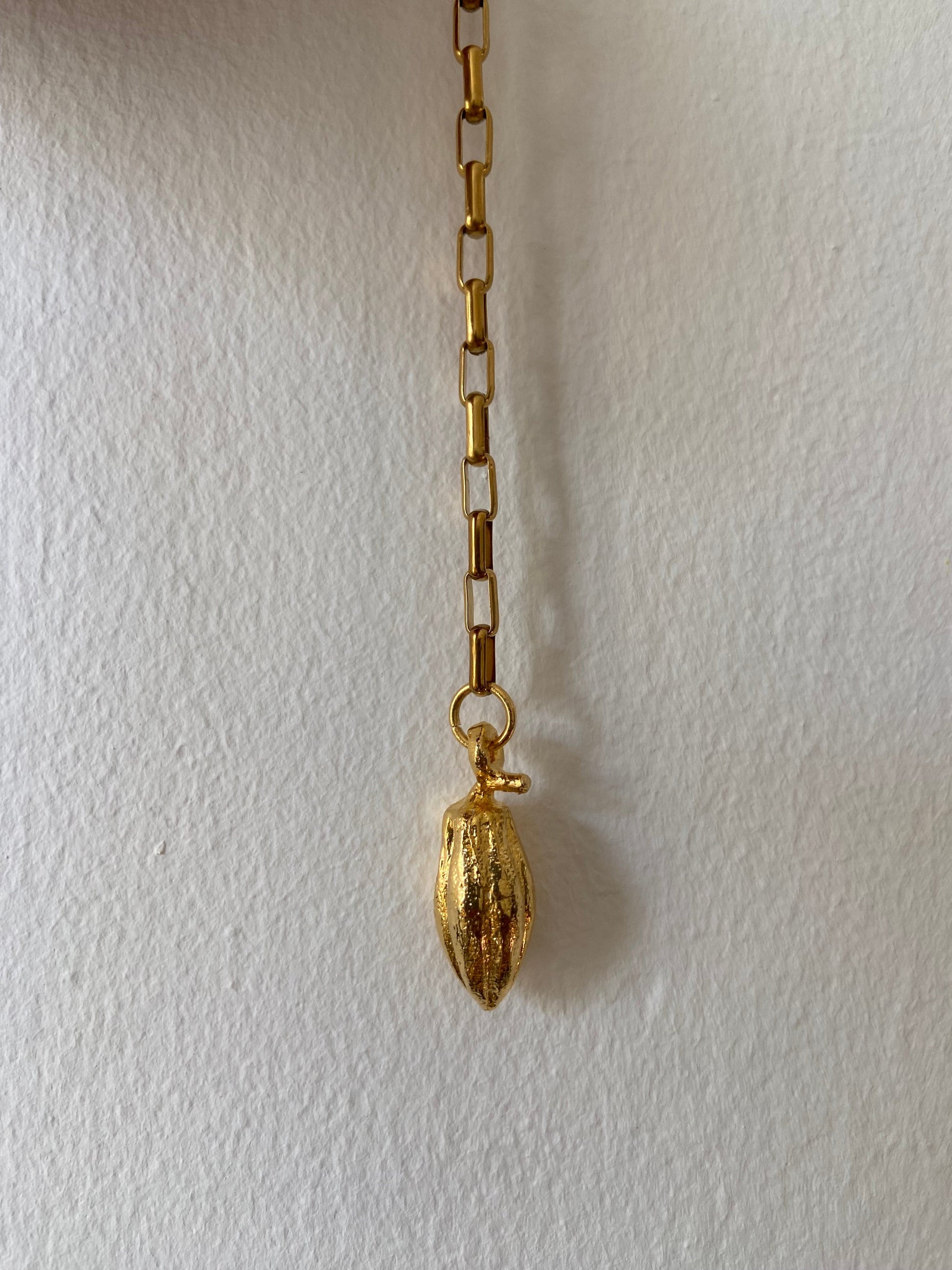A single gold-colored earring with a cocoa bean design, made of brass, displayed against a light background.